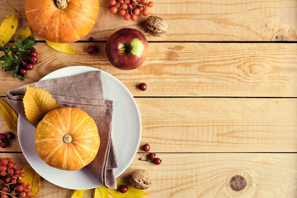 Happy Thanksgiving holiday background. Pumpkins, fallen leaves, plate, apples, red berries on wooden table. Thanksgiving dinner concept. Flat lay, top view, copy space.