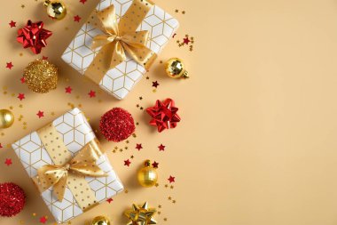 Noel kompozisyonu. Altın kurdeleli hediye kutuları, okuma ve altın top süslemeleri, sarı arka planda konfeti yıldızları. Düz konum, üst görünüm, kopyalama alanı. Noel afişi modeli.