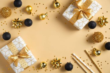 Modern Noel kompozisyonu. Lüks hediye kutularından yapılmış çerçeve, siyah ve altın renkli toplar, sarı arka planda konfeti yıldızları. Düz konum, üst görünüm, kopyalama alanı. Sezonluk tebrik kartı şablonu.