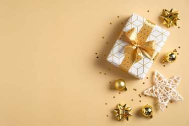 Lüks Noel kompozisyonu. Altın kurdeleli hediye kutusu, top süslemeleri, yıldız, sarı arka planda konfeti. Düz konum, üst görünüm, kopyalama alanı. Sezonluk tebrik kartı modeli.