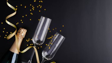 Noel kutlaması konsepti. Noel şampanyası bardakları ve siyah arka planda ışıl ışıl altın konfeti olan şarap şişesi. Xmas tebrik kartı modeli
