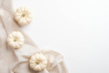 Sonbahar kompozisyonu. Beyaz masa, balkabağı süslemeli ve bej kumaşlı. Düz yerde, üst tarafta. İskandinav, higge, konforlu ev kavramı