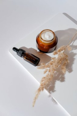 Doğal nemlendirici krem, serum yağı şişesi, beyaz kürsüde kurumuş çiçek. Organik cilt bakım ürünleri