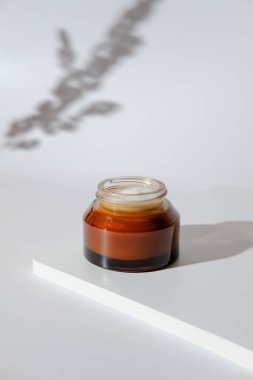 Beyaz kürsüde kehribar cam kavanoz nemlendirici doğal krem. Organik kozmetik ürünleri, cilt bakımı.