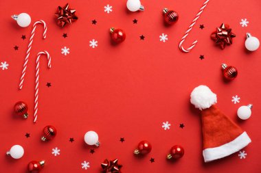 Kırmızı arka plandaki kırmızı Noel süslemesinin çerçevesi. Noel mücevherleri, şeker kamışları, Noel Baba şapkası, konfeti. Düz konum, üst görünüm, kopyalama alanı.