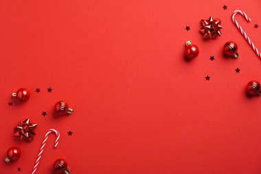 Noel kompozisyonu. Kırmızı Noel süsleri ve kırmızı arka planda şeker kamışları. Düz konum, üst görünüm, kopyalama alanı. Yeni yıl tebrik kartı modeli, pankart şablonu.
