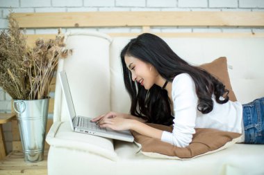 Genç ve güzel bir kadın evde dizüstü bilgisayar kullanıyor..