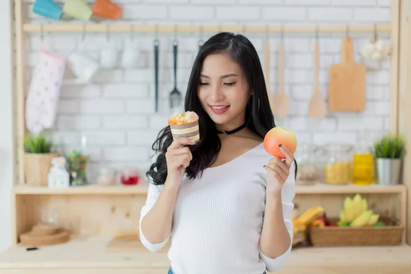 Beautiful young woman making a choice between a cake and apple