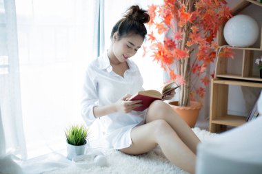 Evdeki pencerenin yanında kitap okuyan güzel genç bir kadın.