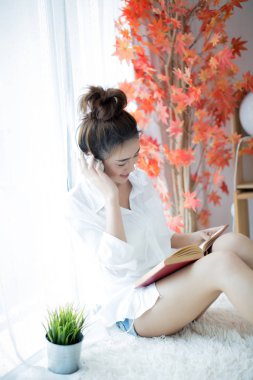 Evdeki pencerenin yanında kitap okuyan güzel genç bir kadın.