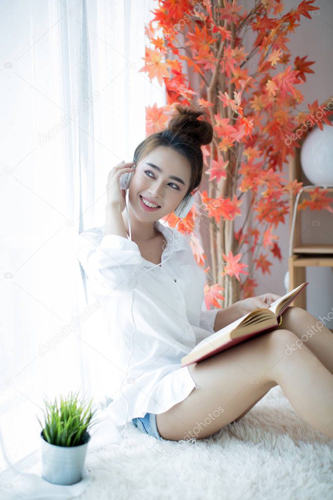 Beautiful young woman reading book near window at home