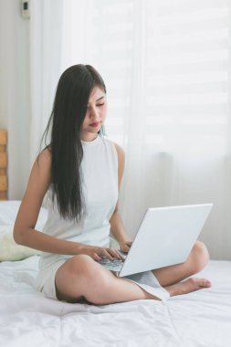 Asyalı kadınlar odada bir yatakta dizüstü bilgisayar ile oynamak