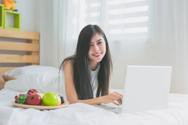 Asian women play with laptop on a bed in the room