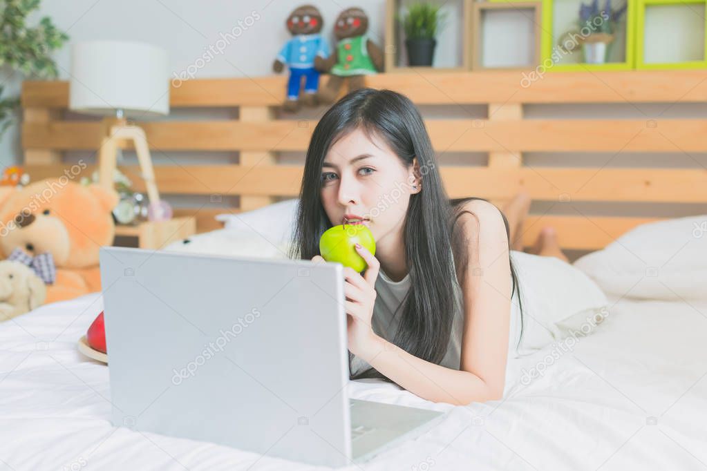 Asian women play with laptop on a bed in the room
