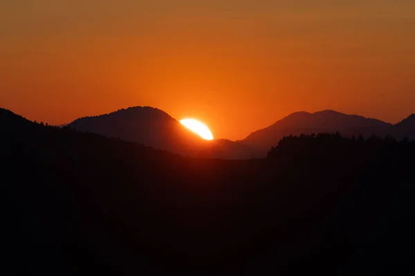 Сияющее солнце садится между холмами на глубоко оранжевом освещенном небе — стоковое фото
