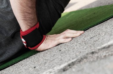 Closeup side view of a mans right hand with wrist band doing push ups on green mat clipart