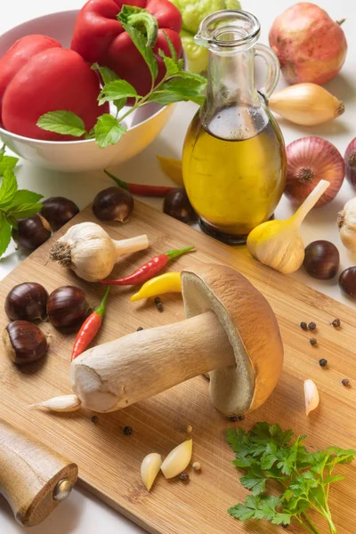 Assorted selection of nature's gifts - mushroom, chestnuts, spices, paprika, garlic, onions, chayote, pomegranate and olive oil on a table with cutting board
