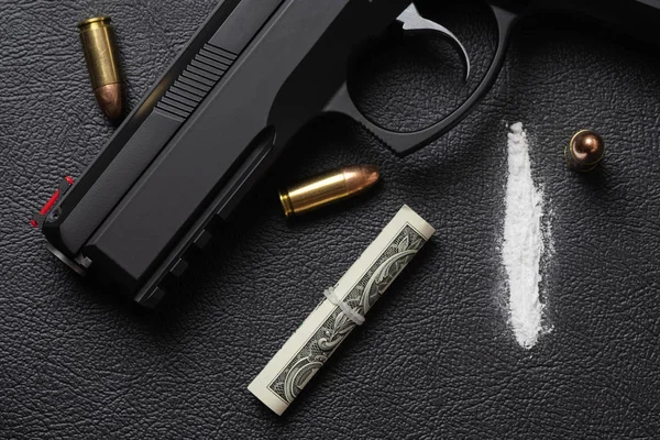 Dollar bill scroll, cocaine powder, pistol and three bullets on black surface — Stock Photo, Image