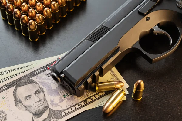Semi-automatic pistol and bullets on dollar banknotes laid out on black table