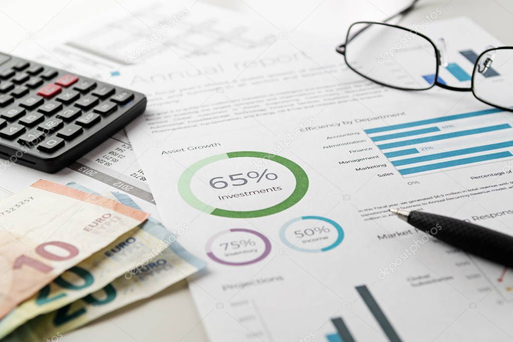 Mockup investment financial charts report sheet with visible pen, calculator, eyeglasses and euro banknotes. Accounting, business, finance, tax and office concepts.