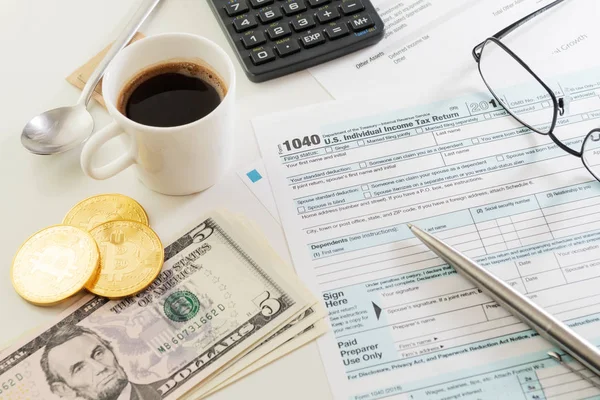 ABD bireysel gelir vergisi beyannamesi formu 1040 Kupası ile espresso, kalem, hesap makinesi, Gözlük, doları banknot ve Bitcoin para beyaz masada. Vergi, muhasebe, işletme, finans ve office kavramları.
