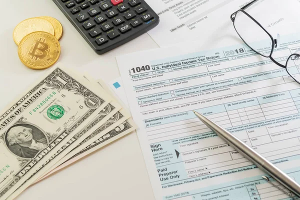 ABD bireysel gelir vergisi beyannamesi formu 1040, hesap makinesi, Gözlük, bazı doları banknot ve Bitcoin cryptocurrency paralar. Vergi, muhasebe, varlıkları, finans ve office kavramları.
