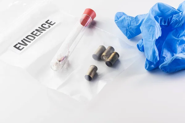 Closeup of 9 mm bullet cases in evidence bag, fibres in glass tube and blue glove isolated on white background. Crime, forensic science, investigation and violence concepts.