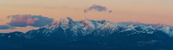 Majestic view of snowcapped alpine peaks of Karawanks and Krvavec ski resort slopes in Slovenia right before sunset. Alps, mountaineering, travel, skiing, winter sports and beautiful nature concepts.