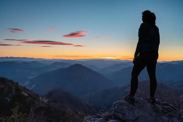 Silhouette of female hiker standing on top of the hill and enjoying the view of landscape after sunset. Hiking, achievement, lifestyle and nature concepts.