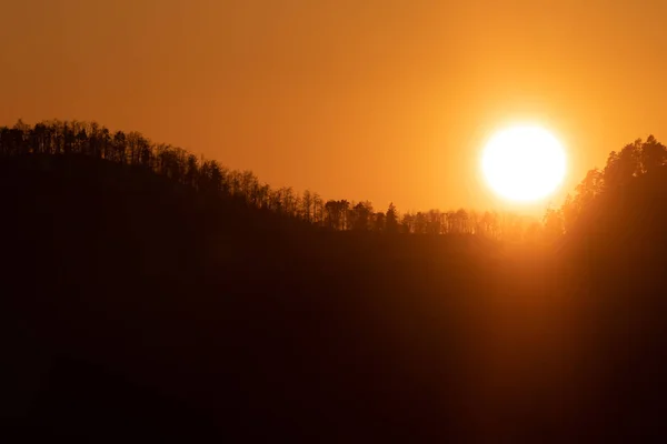 Cielo arancione con sole splendente che tramonta dietro la collina alberata — Foto Stock