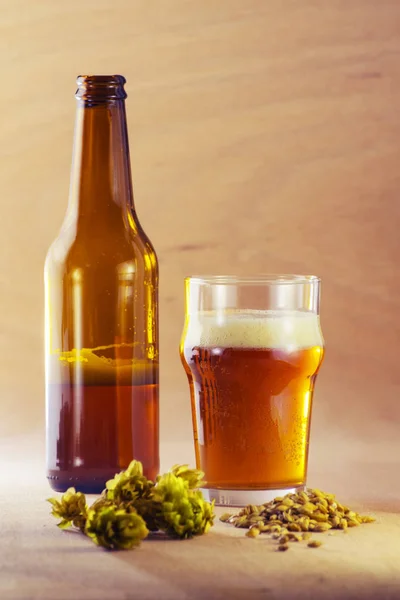 Flasche und Glas Bier mit Gerste und Hopfen auf Holzgrund — Stockfoto