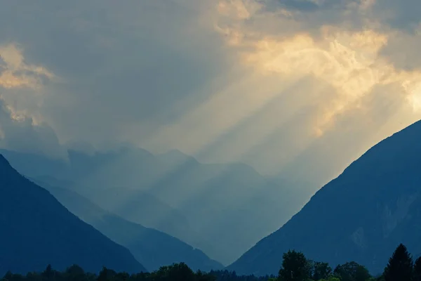 Himmelska gyllene ljusstrålar som lyser genom moln ner till dal och berg — Stockfoto