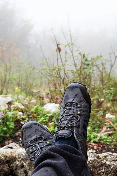 Crossed hiker\'s feet with gray trekking shoes and foggy forest in background