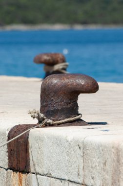 Arka planda mavi deniz olan beton iskeledeki eski ve paslı demirleme bölmesi. Yelkencilik, tatil, seyahat, turizm ve deniz faaliyetleri kavramları