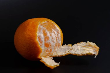yarısı soyulmuş mandarin siyah zemin üzerinde sulu