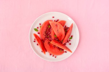 Karpuz ve nar salatası bir beyaz plaka ve pembe kumaş arka plan. 