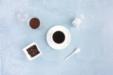 Natürmort siyah kahve fincan, kahve çekirdekleri, kahve ve beyaz şeker mavi beton zemin üzerine yer..