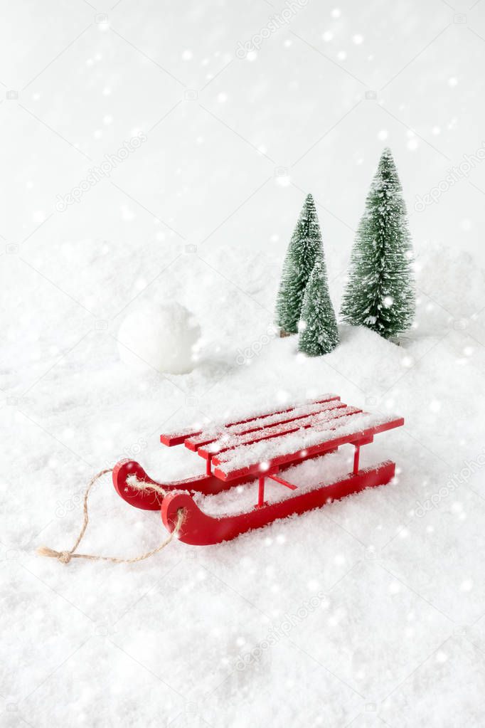 Winter Scene with a red wooden sledge, snow, a giant snowball, fir trees and snowfall. 
