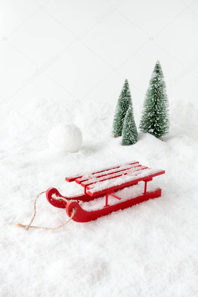 Winter Scene with a red wooden sledge, snow, a giant snowball and fir trees.