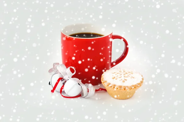 Sade kahve, beyaz jingle bells, gümüş metalik şerit, börek ve kar taneleri ile dekore edilmiş kırmızı kupa dolu.