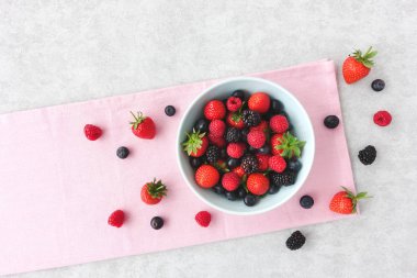 Taze yaz meyveleri pembe kumaş ve ile lots-in kopya alanı gri arka plan üzerinde mavi bir kabın içinde çeşididir. Üstten görünüm.