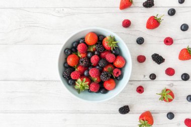 Taze yaz meyveleri kopya alanı ile beyaz ahşap zemin üzerinde mavi bir kabın içinde çeşididir. Üstten görünüm.