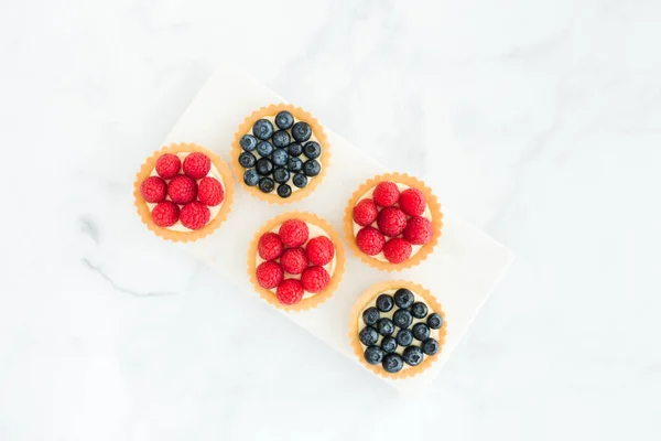 Ev yapımı yaban mersini ve ahududu ve beyaz mermer tahta ve arka plan üzerinde tartlets. Üstten görünüm.