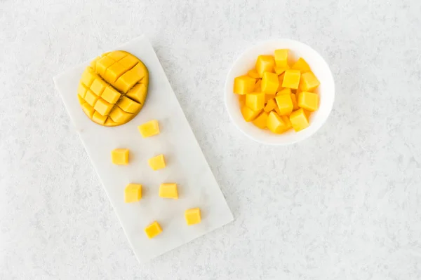 Kesme mango üstten görünüm yarısı ve mango cubes beyaz mermer kesme tahtası ve beyaz kase.