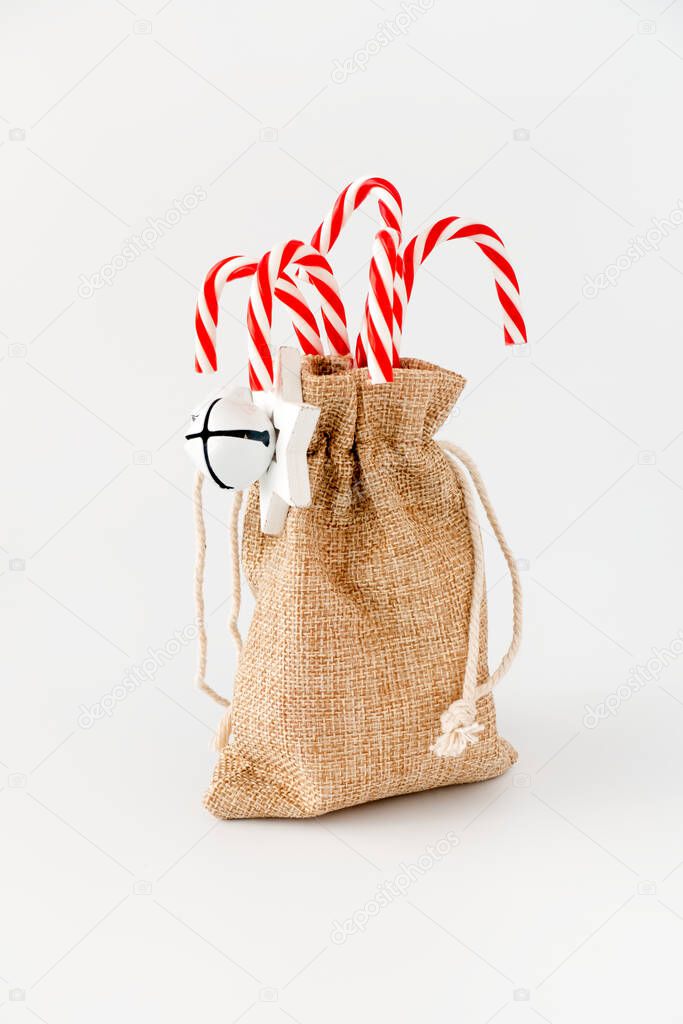 Red candy canes in jute sack with jingle bells and Christmas star isolated on white. Low angle view.