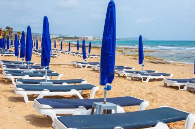 Şemsiyeler ve güneş yatakları mevsimin başında kumlu sahilde. Boş kumsal. Terk edilmiş dinlenme alanları. Ayia NAPA, Kıbrıs