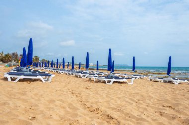 Şemsiyeler ve güneş yatakları mevsimin başında kumlu sahilde. Boş kumsal. Terk edilmiş dinlenme alanları. Ayia NAPA, Kıbrıs