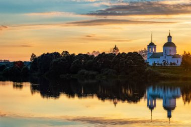 Gün batımında gölün sularında ormanın ve kilisenin yansıması. Sıcak bir akşamda yaz manzarası.