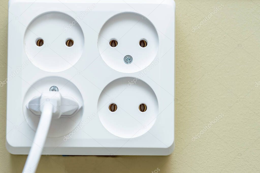Electrical socket with four sockets. one of the outlets has an electric plug on a beige background close-up.
