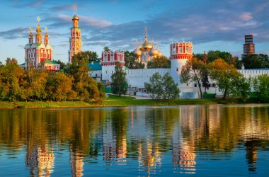 Gün batımında gölde yansıması olan Novodevichy Manastırı. Altın kubbeli ünlü Moskova simgesi ve Park göletinin sularındaki manzaranın yansıması bulutlu mavi gökyüzünün arka planına karşı..